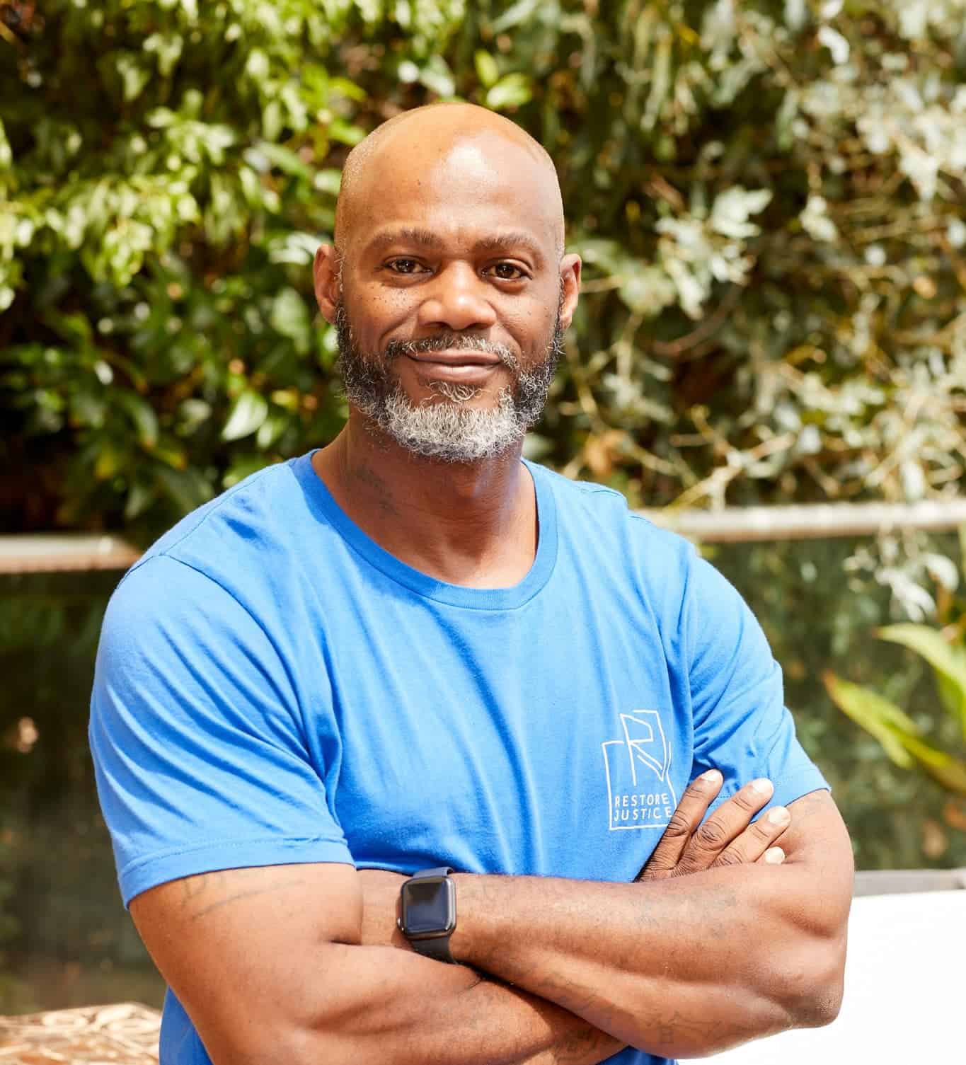 Smiling black man with crossed arms and a restore justice logo t-shirt